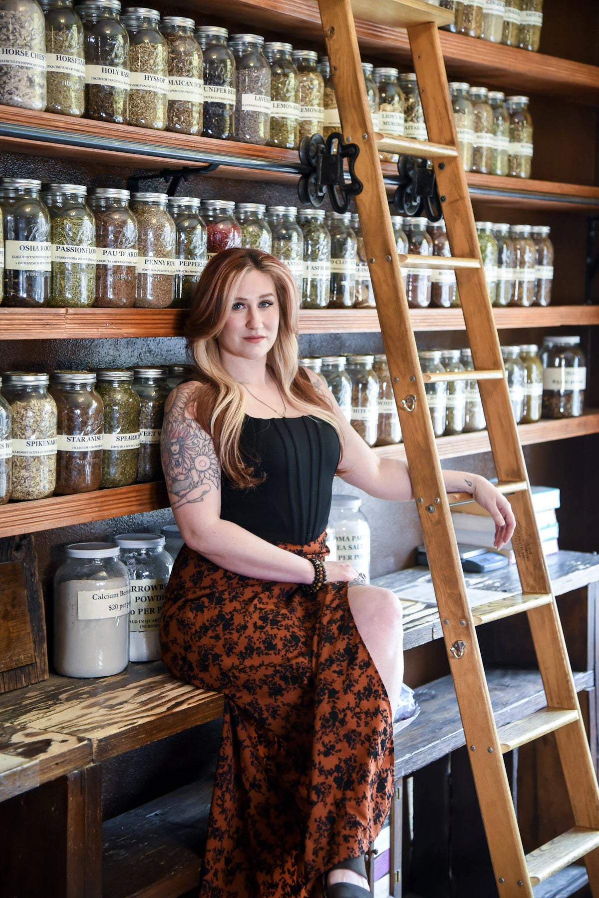 Woman sitting on a wooden shelf with jars of bulk herbs in a store setting