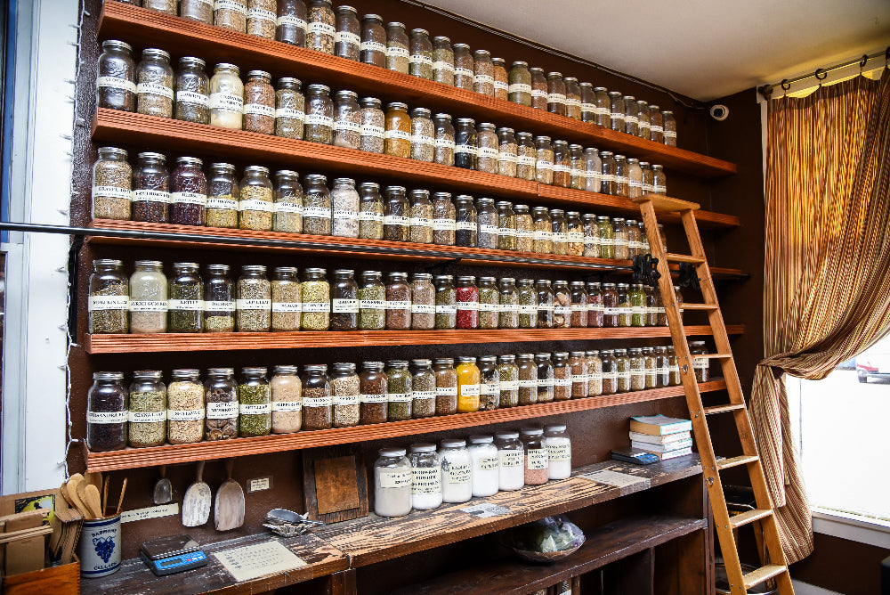 Shelves filled with various jars of loose herbs and teas at Wise Roots Apothecary, and a ladder in a room with curtains.